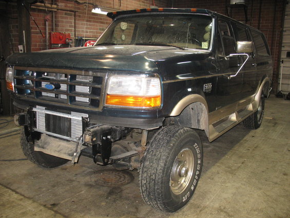 Dark green Ford F-Series truck with tan trim, missing front bumper, and exposed intercooler