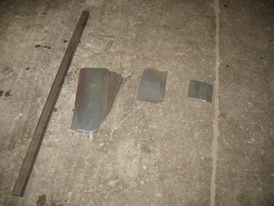 Metal bar, stack of curved metal plates, and two small metal squares on a concrete floor