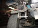 1995 Ford C-350 (Centurion Conversions) - Close-up of a custom suspension modification, showing a C-clamp securing a metal bracket near a tire.