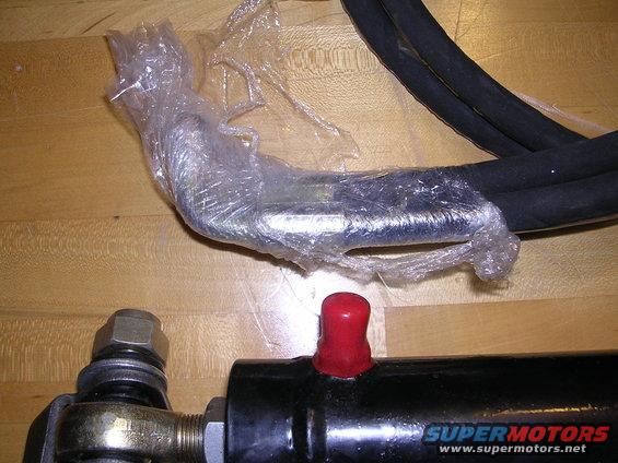 Hydraulic hose and cylinder parts wrapped in plastic, with a red cap on the cylinder