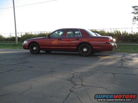 Side view of a red 2000 Ford Crown Victoria parked on cracked asphalt