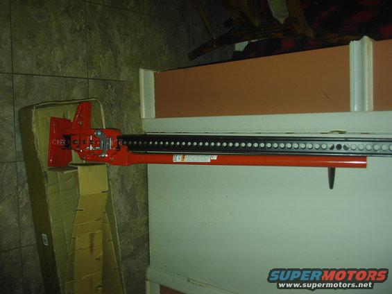 Red hi-lift jack with black lifting bar, partially in cardboard box