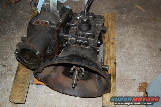 Black transmission and transfer case assembly on wooden blocks. Visible splined shaft and shifter