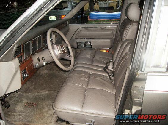 Interior view of a car with plush leather seats, wood trim dashboard, and steering wheel. Another vehicle is visible through the window