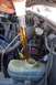 1990 Ford Bronco - Amber fluid is poured into a vehicle's reservoir from a glass tube in the engine bay.