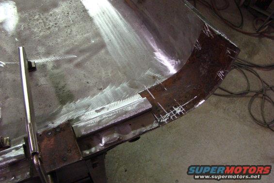 Metal panel with grinding marks and chalk lines, showing a curved section and a straight edge with a clamp
