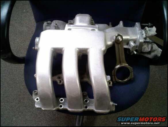 Silver aluminum intake manifold and connecting rod on a dark chair