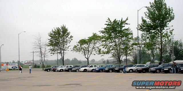 Several police cars parked in a lot, some with hoods up. Two people stand near the front