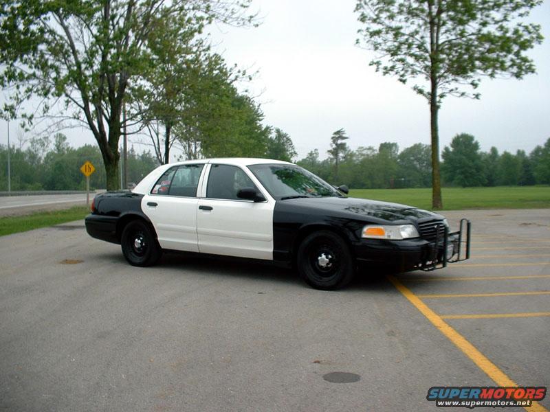 Two-tone police car, black front and white rear, parked in a lot with yellow lines. Push bar on front