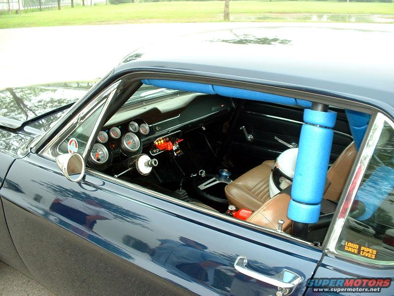 Interior view of a dark blue classic car with a roll cage, racing seats, and many gauges on the dashboard