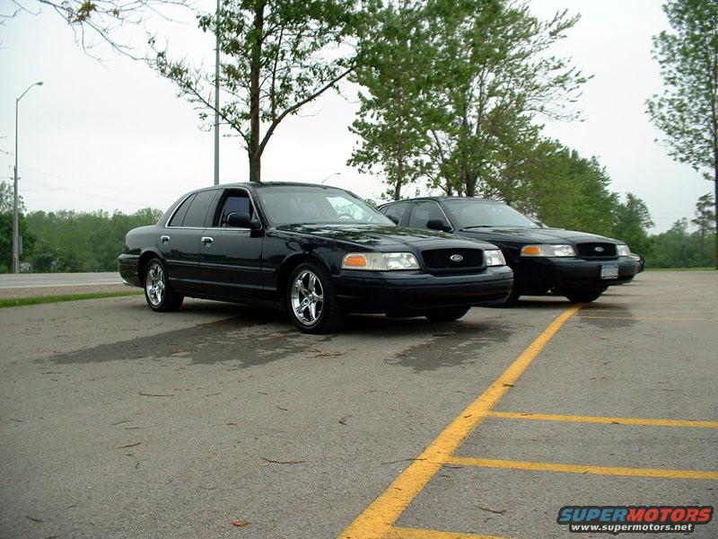 Two black Ford Crown Victorias parked in a lot, one in front of the other