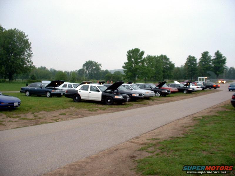 Police car with hood up, parked on grass next to other vehicles