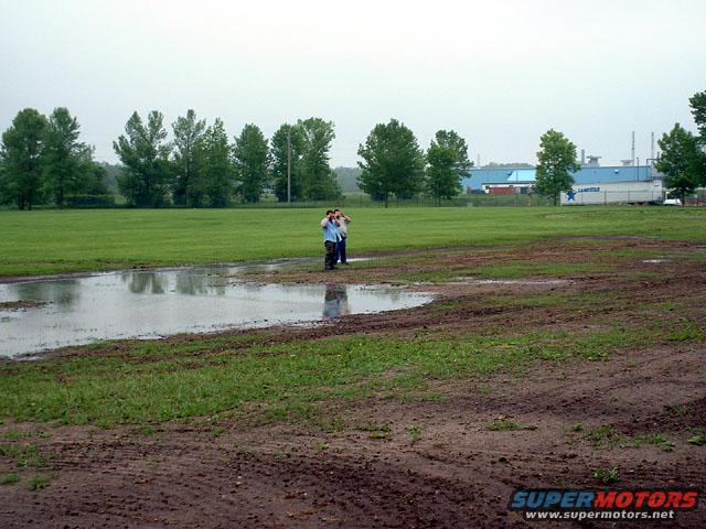 Muddy field with puddles and distant industrial buildings