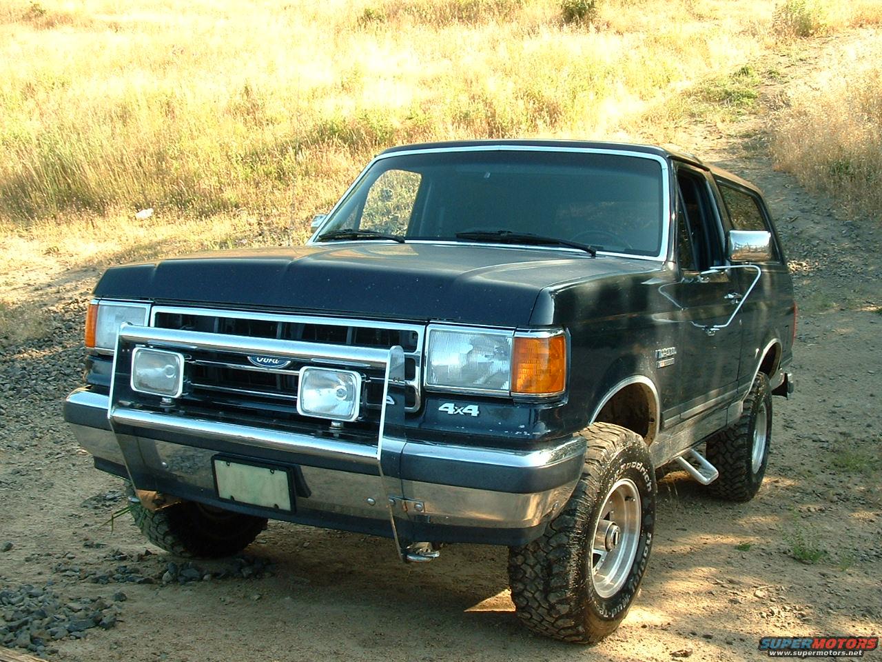 Dark blue Ford Bronco with a chrome grille guard and off-road tires parked on a dirt road