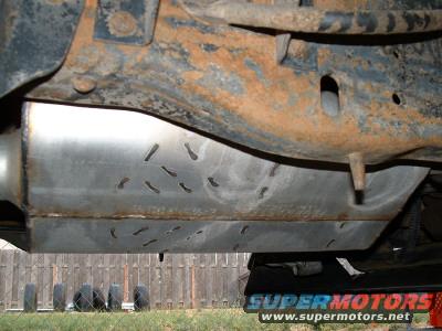 Undercarriage with rusted frame and metal skid plate with cutouts