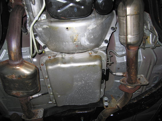 Underside view of a vehicle's transmission pan, exhaust pipes, and catalytic converter