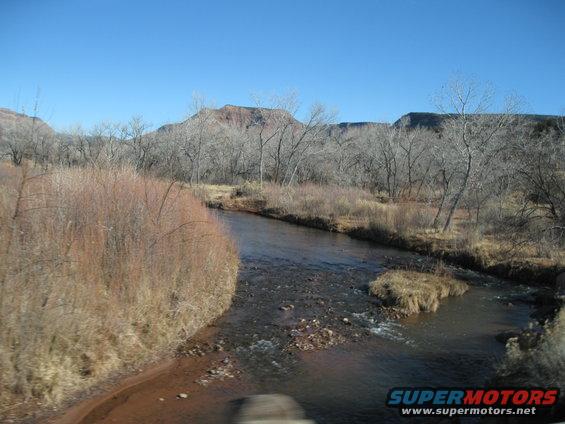 River flowing through a landscape with bare trees and hills under a clear blue sky