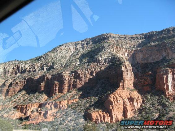 Mountain landscape with red rock formations and sparse vegetation under a clear blue sky