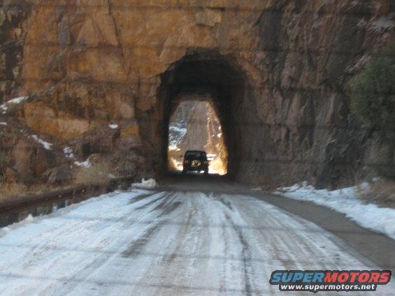 Dark SUV seen from behind driving on a snow-covered road through a rock tunnel
