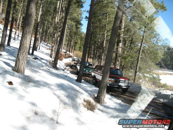 Red and white Ford Bronco driving on a snowy road, front 3/4 view