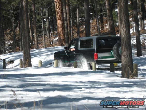 1993 Ford Bronco driving through snow in a wooded area, kicking up snow