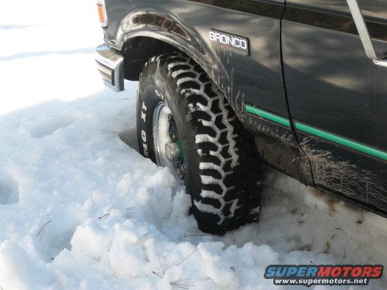 Close-up of a 1993 Ford Bronco's front tire stuck in snow