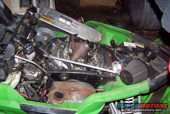 Green snowmobile engine compartment with exposed engine, air filter, and various hoses and wires