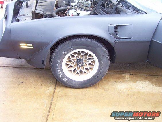 Front fender and wheel of a 1978 Pontiac Trans Am, hood is open showing engine components