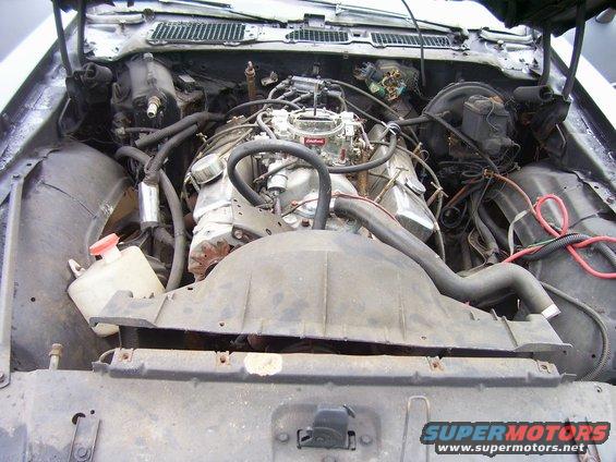 Engine bay with V8 engine and carburetor. SuperMotors.net logo visible