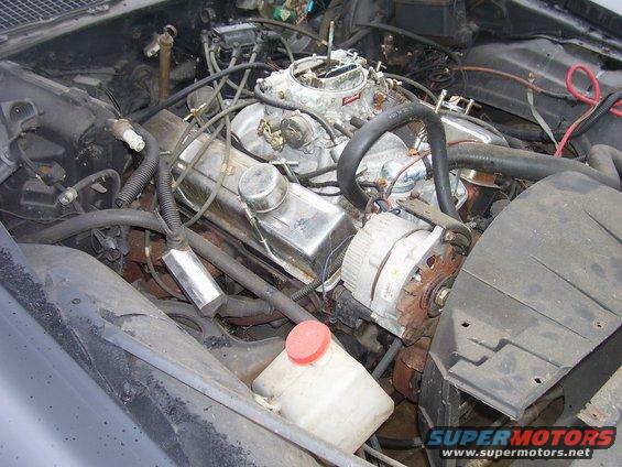 Engine bay view showing V8 engine, carburetor, alternator, and hoses
