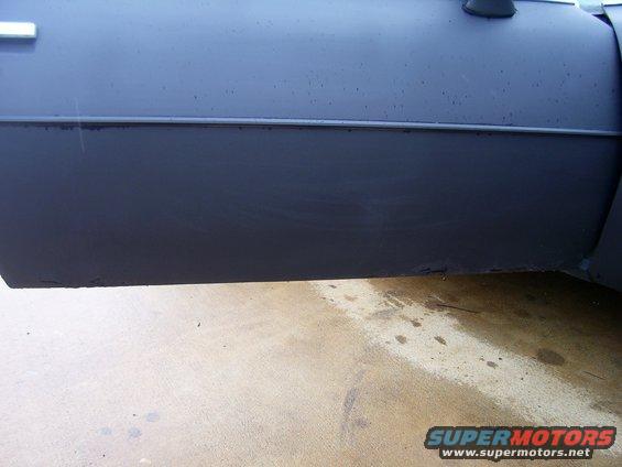 Side view of a dark colored car's door and lower body panel. Some scuff marks and rust are visible