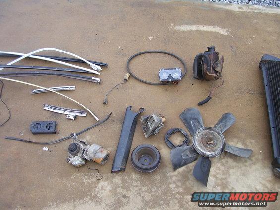 Assorted car parts including trim, fan, radiator, and engine components on concrete