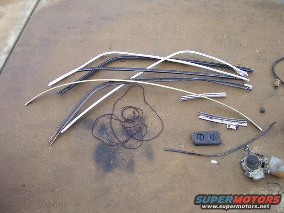 Assorted car trim pieces, a black wire bundle, and a windshield wiper motor assembly laid out on a concrete surface