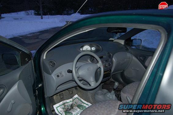Interior of a green car, showing the dashboard, steering wheel, and seats. A stop sign is visible outside