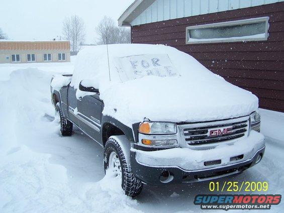 GMC pickup truck covered in snow with 'FOR SALE' written on windshield. Date stamp shows 01/25/2009
