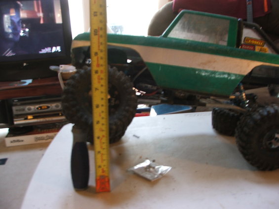 Green and white RC truck body with large tires, next to a measuring tape