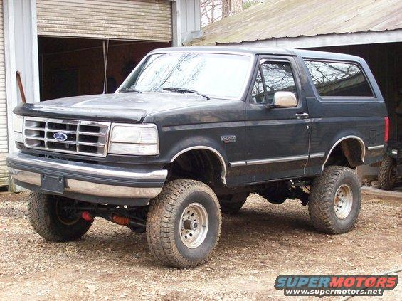 Black 1992 Ford Bronco with lifted suspension and large tires parked in front of a garage