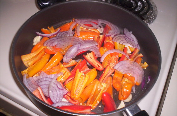 Chopped bell peppers and red onion in a frying pan on a stovetop