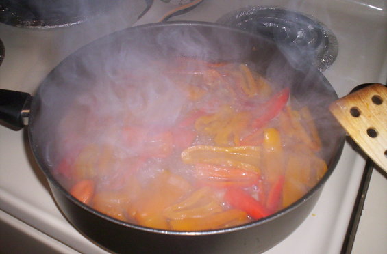 Peppers cooking in a frying pan on a stovetop, with steam rising