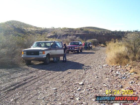 Two-tone Ford Bronco on a dirt road with other vehicles behind it