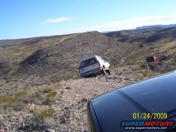 White SUV climbing a rocky hill, red SUV in background. Shot from another vehicle
