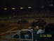 1996 Ford Bronco - Monster trucks are prepared for an event in an indoor arena, with a crowd watching from the stands.