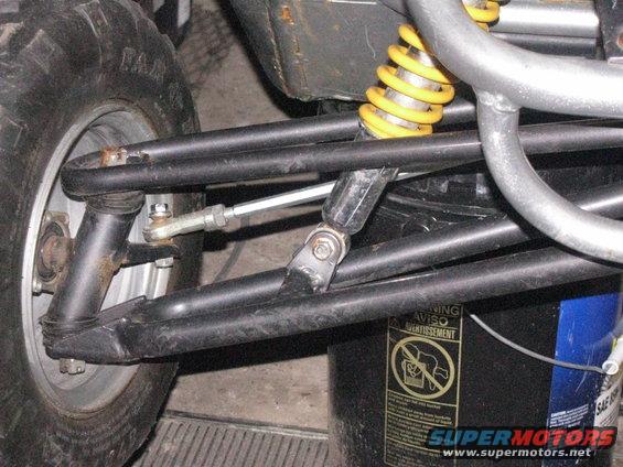 Go-kart rear suspension with yellow shock absorber, black control arms, and tire. Black bucket with warning labels visible