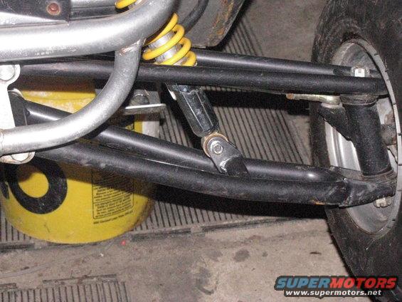 Close-up of go-kart front suspension with yellow shock absorber and black A-arms. A yellow bucket is visible behind the suspension