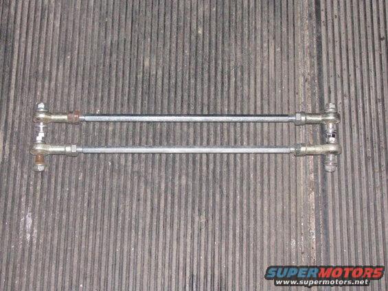 Two metal rods with threaded ends and ball joints, laid out horizontally on a ribbed surface