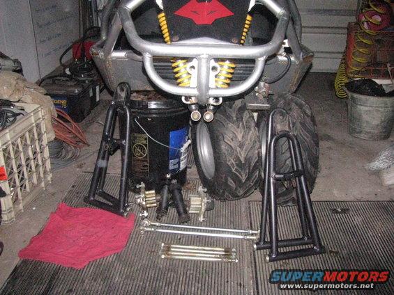 Go-kart frame with yellow shocks, silver bumper, and tires, surrounded by suspension parts and a red rag
