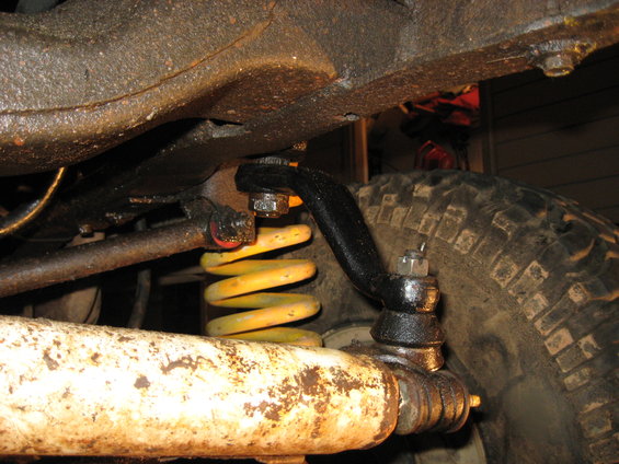 Close-up of vehicle suspension with yellow coil spring and steering linkage