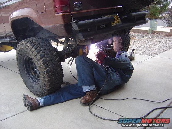 Man welding under a Ford Bronco II. The vehicle has large off-road tires and a custom bumper