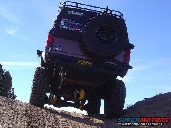 Rear view of a lifted Ford Bronco on a dirt hill, with a spare tire mounted on the back and various stickers on the tailgate
