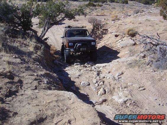 Brown off-road SUV with roof rack and winch driving on a dirt trail with rocks